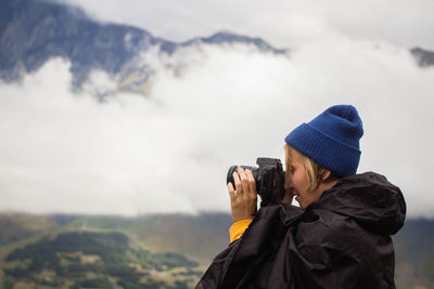 Woman photographing on mountain against sky