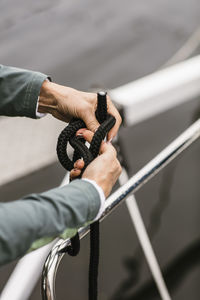 Cropped hands of senior female instructor tying rope on yacht's railing