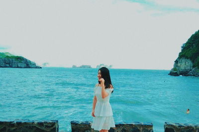 Woman standing on rock by sea against clear sky