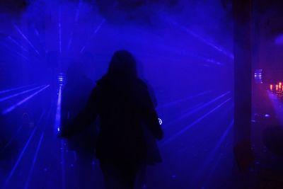 Rear view of silhouette woman walking on illuminated street at night