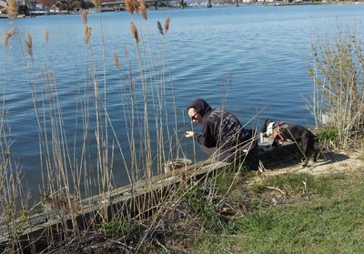 Side view of woman with dog sitting on retaining wall by lake