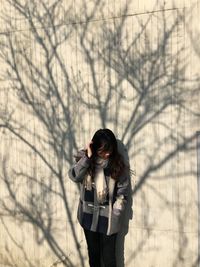 Woman with hand in hair standing by wall