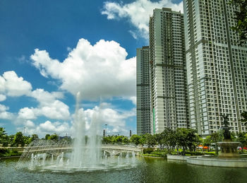 Fountain in city against cloudy sky