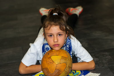 The girl is lying on the floor with a fan scarf and a ball under her face.