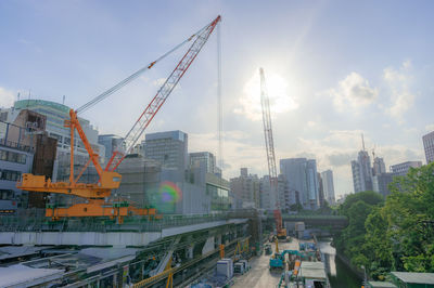 Cranes by buildings against sky in city