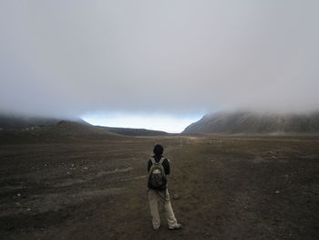 Rear view of backpack woman standing on field against cloudy sky