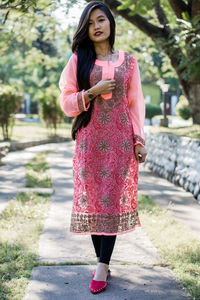 Full length of woman standing on pink phone outdoors