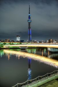 Illuminated buildings by river against sky at night