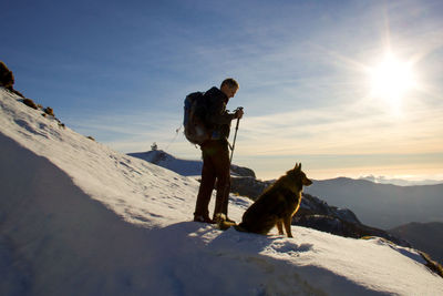 Man with dog standing on snow against sky