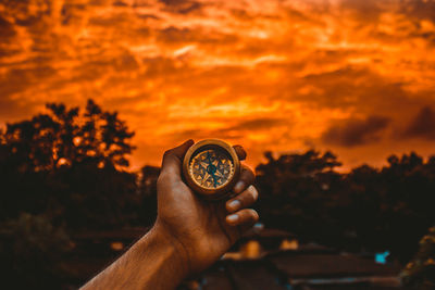 Close-up of hand holding orange against sky during sunset