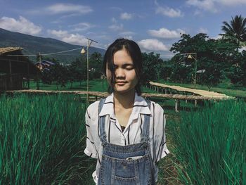 Young woman with eyes closed standing amidst plants on field against sky