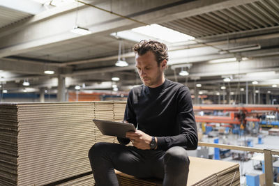 Businessman using digital tablet while sitting on cardboard stack