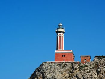 Low angle view of lighthouse against buildings against clear blue sky