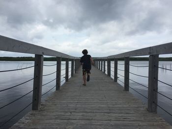 Rear view of boy running on bridge against sky