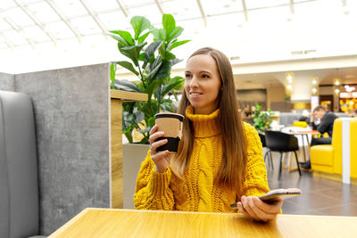 Young woman using phone while sitting on table