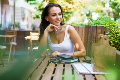 Satisfied young woman in white t-shirt sits at table of an outdoor street cafe.