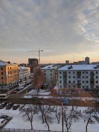 Snow covered buildings against sky during sunset