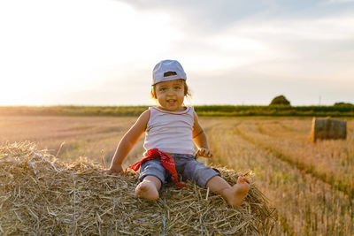 Boy child in a light t-shirt sitting on a haystack during the sunset in summer