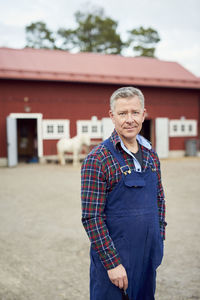 Portrait of mature farmer standing on field against barn