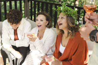 Cheerful women with drinks sitting by young man at patio in back yard