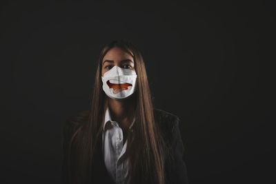 Executive young woman wearing medical mask with drawn smile on black background