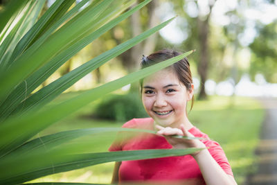 Portrait of smiling young woman holding plant at public park