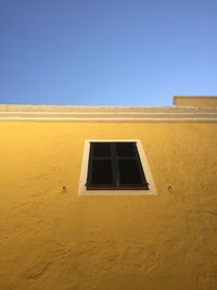 Low angle view of yellow building against clear blue sky