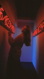 Side view of woman standing against illuminated wall at home