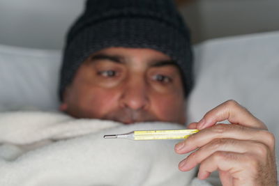 Man checking temperature while lying on bed at home