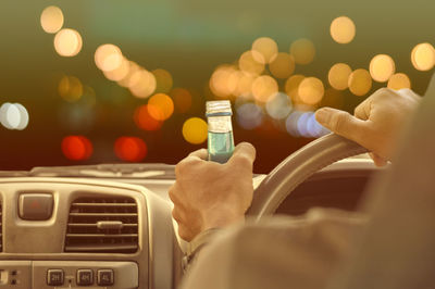 Close-up of man holding bottle while driving car at night