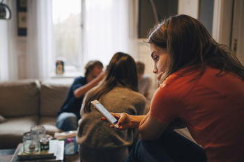 Girl using smart phone while sitting with friends in living room