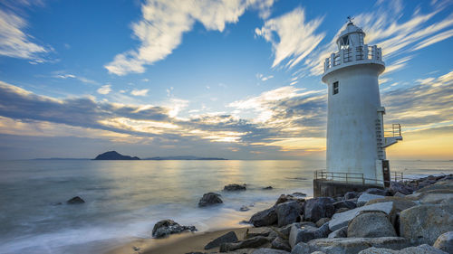 Lighthouse by sea against sky during sunset