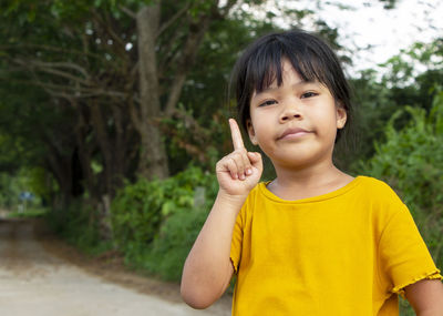 Portrait of a cute little girl dress casually standing and pointing up in the natural background. 