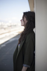 Side view of young woman standing against sky