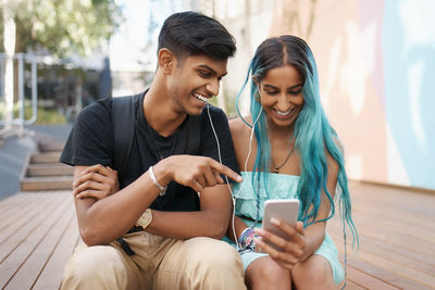 Smiling friends using mobile phone while sitting at home