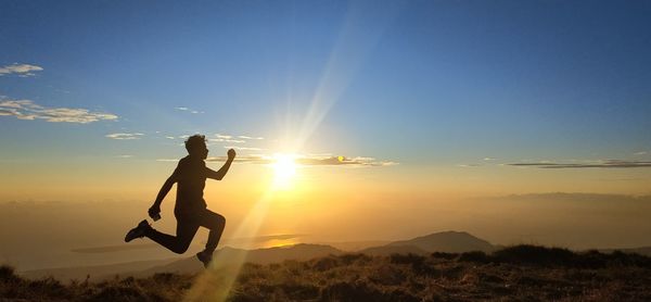 A man was jumping over a very beautiful mountain at sunset