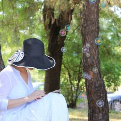 Side view of woman using mobile phone while sitting by bubbles and tree trunk