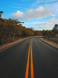 Empty road amidst trees against sky