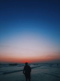 Rear view of woman walking on beach against clear sky during sunset