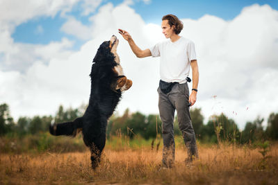 Man playing with dog while standing on land against sky