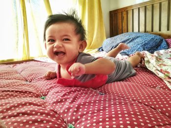Cute baby boy laughing while lying on bed at home
