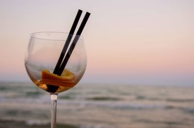 Close-up of leftovers in wineglass against sea during sunset