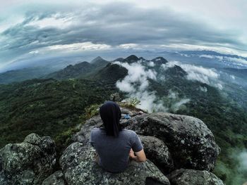 Rear view of man sitting on rock against mountain