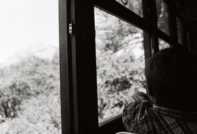 Rear view of boy looking through window