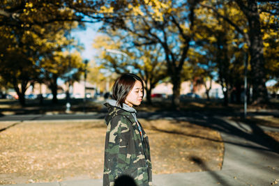 Side view of woman standing against trees at park during autumn
