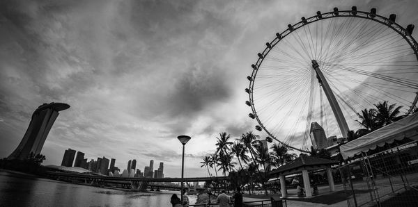 Low angle view of ferris wheel in city against cloudy sky