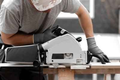 A young man is sawing a board with an electric saw.