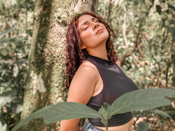 Young woman looking up against tree trunk