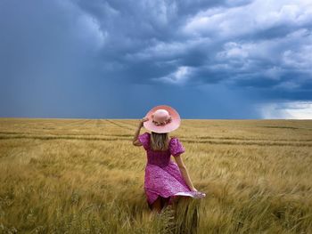 Rear view of woman with hat standing on field against sky