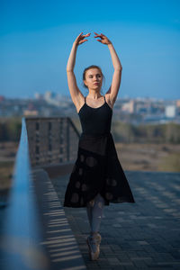 Full length portrait of young woman dancing against sky